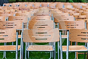 Wooden chairs stand outside in the park in the rain. Empty auditorium, green grass, waterdrops, closeup