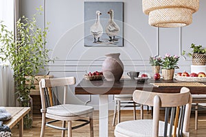 Wooden chairs at table with flowers in natural dining room interior with poster and lamp. Real photo