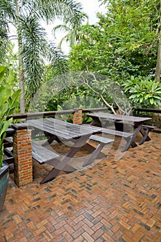 Wooden chairs and table set at balcony in a green plant garden.