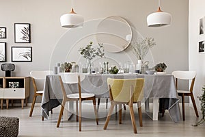 Wooden chairs at table with tableware in dining room interior with lamps and round mirror.