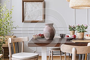 Wooden chairs at table with vase and flowers in grey dining room interior with poster. Real photo