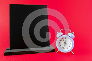 Wooden chalkboard mockup or wooden frame, alarm clock 12 hours on red surface. Dark information board template, sign