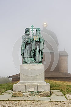 Wooden chapel and statue of Saint Cyril and Methodius on summer foggy day in Beskid mountains in Czech Republic