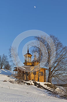 Wooden chapel on a sunny winter day on a background blue sky with the moon