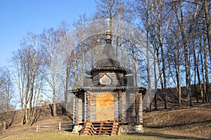 A wooden chapel surrounded by bare trees against a sky