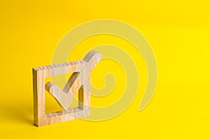 A wooden checkmark in the box on a yellow background. The concept of suffrage, voting in elections. Election of the President