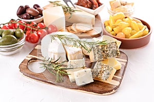 Wooden cheese board with variety of cheeses served with olives, cherry tomatoes, pickled baby peppers