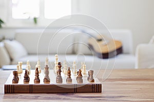 Wooden chessboard on a table in a bright living room with couch and guitar in the background