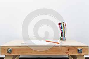 Wooden child drawing table with color pencils by the white wall