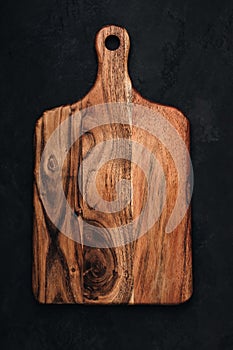 Wooden chopping board on dark stone background, top view