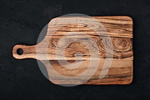 Wooden chopping board on dark stone background, top view