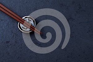 Wooden chopsticks and chopstick rest on dark stone background. Top view.