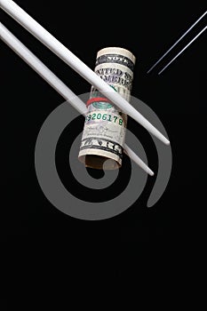 Wooden chopsticks hold an American dollar bill