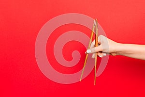 Wooden chopsticks holded with female hands on red background. Ready for eating concepts with empty space