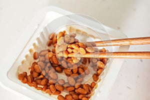 Wooden chopsticks holding Japanese natto beans on white background top view.