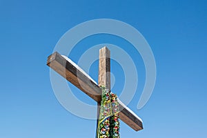 Wooden christian cross with green wreath and blue yellow ribbons on the plain blue sky background, Concept of hope