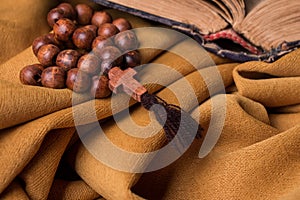 Wooden Christian cross and rosary and old bible on a background of golden fabric drapery.