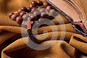 Wooden Christian cross and rosary and old bible on a background of golden fabric drapery.