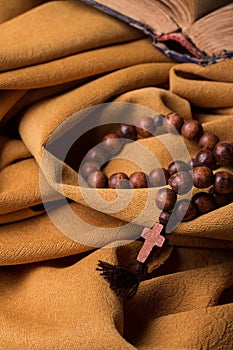 Wooden Christian cross and rosary and old bible on a background of golden fabric drapery.