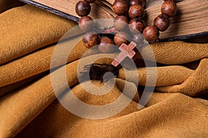 Wooden Christian cross and rosary and old bible on a background of golden fabric drapery.