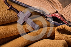 Wooden Christian cross and rosary and old bible on golden fabric drapery. Holy book.