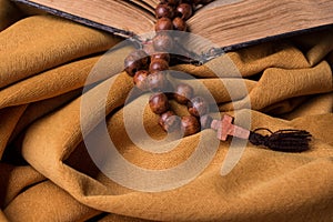 Wooden Christian cross and rosary and old bible on golden fabric drapery. Holy book.