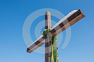 Wooden christian cross with Ukrainian flag color ribbons, yellow and blue, on the plain blue sky background, Concept of