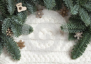 Wooden Christmas decorations lie near the fir branches on a white knitted sweater. Background.