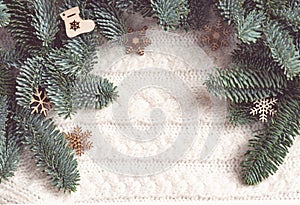 Wooden Christmas decorations lie near the fir branches on a white knitted sweater. Background. Toning pastel