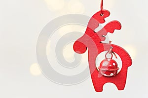Wooden Christmas ornament red deer with bell hanging on white background with golden garland bokeh lights