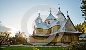 The wooden church is painted yellow with a silver dome. Warm sunny evening