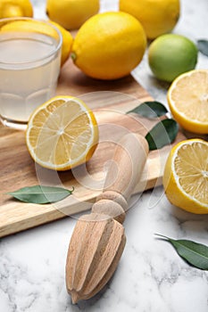 Wooden citrus reamer, fresh lemons and lime on white marble table