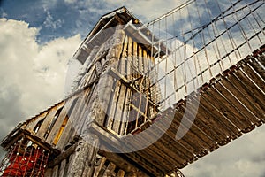 Wooden climbing tower with Net climbing mesh on bridge to another tower and person climbing down mesh tunnel -  perspective