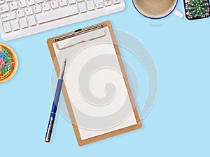 Wooden clipboard with blank paper and pen, keyboard, cactus coffee cup on blue work table. Top view with space for text.