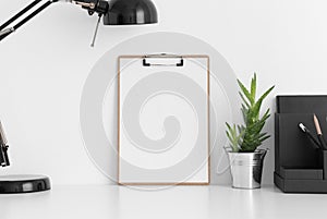 Wooden clipboard mockup wtih a aloe vera in a pot, lamp and workspace accessories on a white table