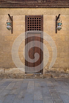 Wooden closed door and Arabic glass street lanterns hanged on a wooden pole in old stone bricks wall