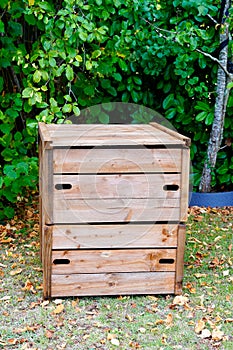 Wooden closed home garden compost bin of organic material composter in back house outdoor