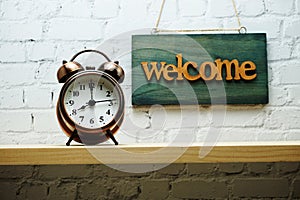 Welcome sign and alarm clock with space copy on white brick wall background