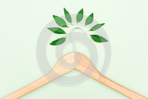 Wooden clothes hanger with green leaves over mint background as a symbol of conscious consumerism, slow fashion