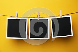 Wooden clothespins with empty instant frames on twine against yellow background. Space for text