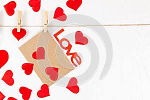 Wooden clothespins hang on a rope on a white background and hold a heart and an envelope. many scattered hearts and the word love