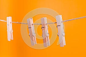 Wooden clothespins hanging on a rope over yellow background.