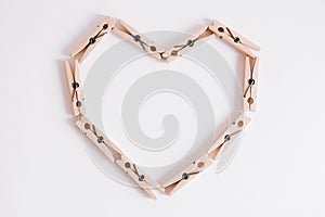Wooden clothespins on white background which are folded in the form of heart icon. View from above