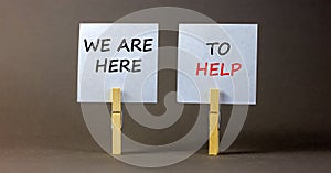 Wooden clothespins with white sheets of paper. Text `we are here to help`. Beautiful gray background. Business concept, copy spa