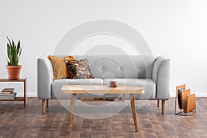 Wooden coffee table in the middle of elegant living room with grey couch and magazine rack on the wooden floor, real photo