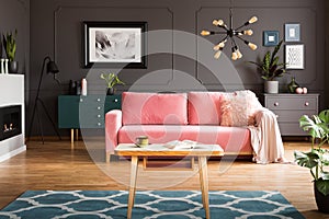 Wooden coffee table with tea cup and open book standing on carpet in dark living room interior with powder pink lounge with fur c