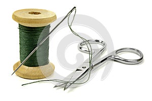 Wooden coil with threads, needle and chromeplated scissors on a white background