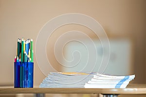 Wooden colorful drawing pencils arranged in plastic jug and stack of copybooks on light copy space background