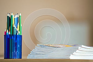 Wooden colorful drawing pencils arranged in plastic jug and stack of copybooks on light copy space background