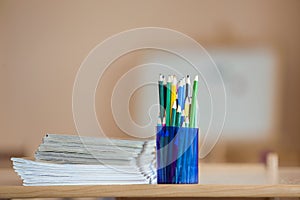 Wooden colorful drawing pencils arranged in plastic jug and stack of copybooks on light copy space background